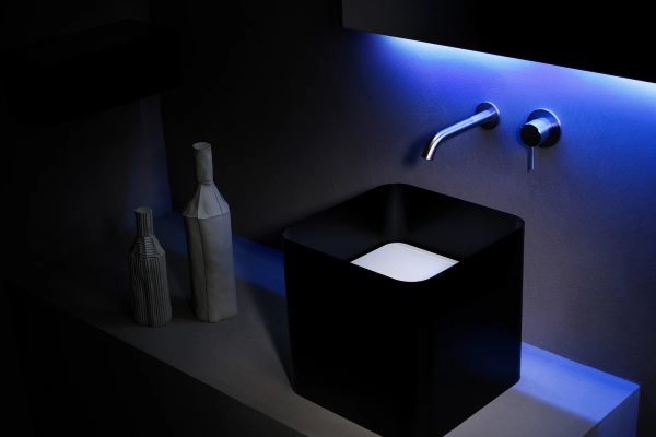 black square sink with modern wall-mounted faucet and blue LED lighting, accompanied by decorative vases