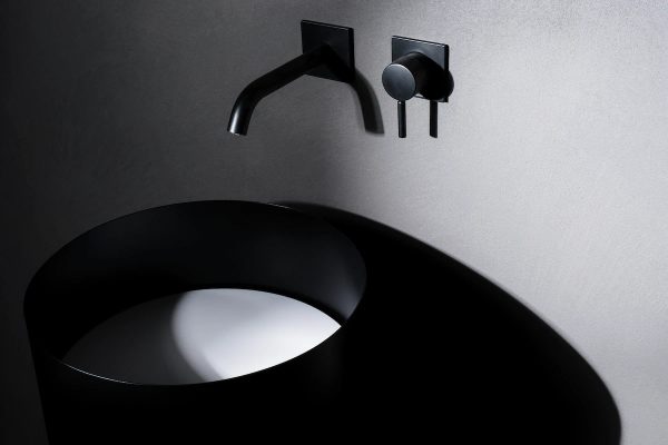 freestanding cylindrical black steel sink with wall-mounted faucet and knob, set in a minimal design context
