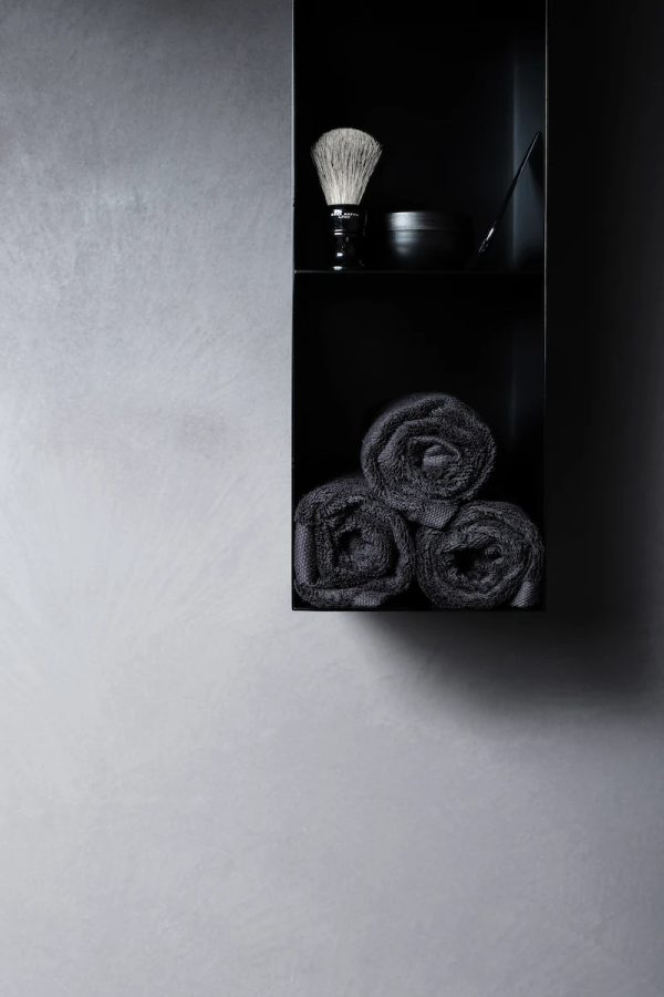 detail of a shelf with luxury bathroom accessories and black towels on a gray wall