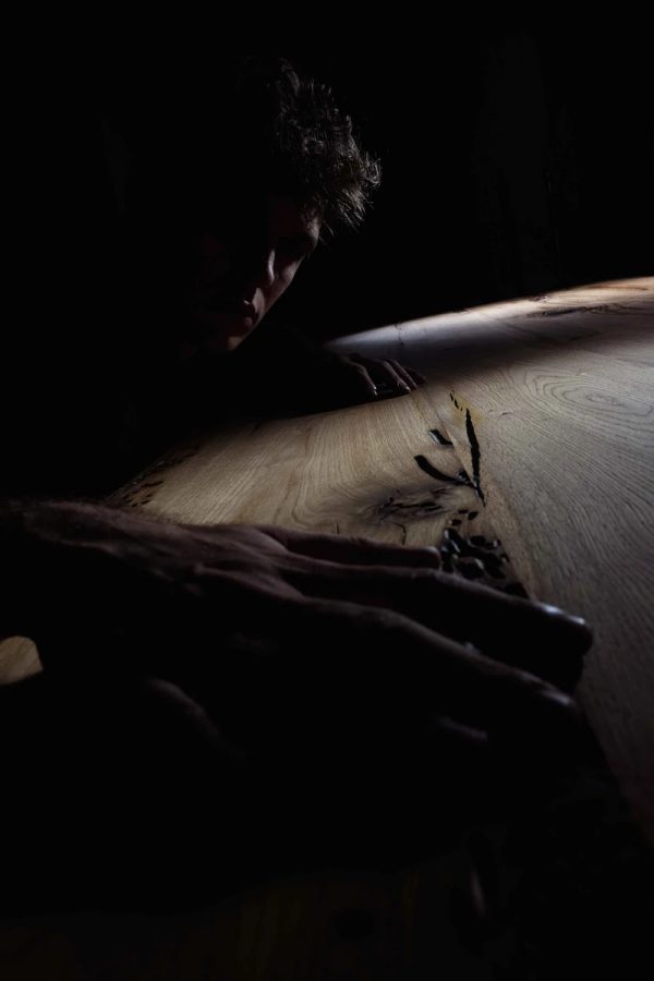 figura che osserva il piano del tavolo in legno di briccole, atmosfera intima e luce teatrale