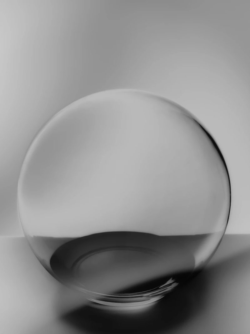 minimalist glass sphere resting on a reflective surface, illuminated by diffused light.