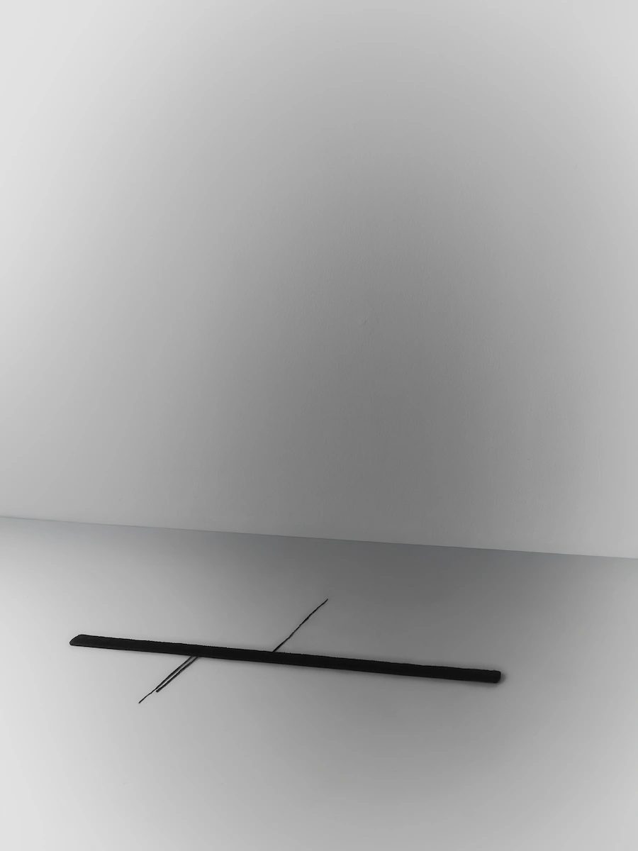 tappeto tessile nero minimalista con filo sottile verticale, composizione orizzontale su sfondo grigio