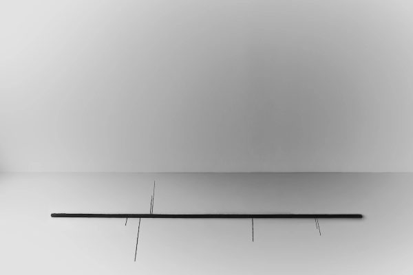 tappeto in seta nero, lungo e sottile, posato orizzontalmente su un pavimento chiaro in un ambiente minimalista, con frange sottili che si estendono da esso