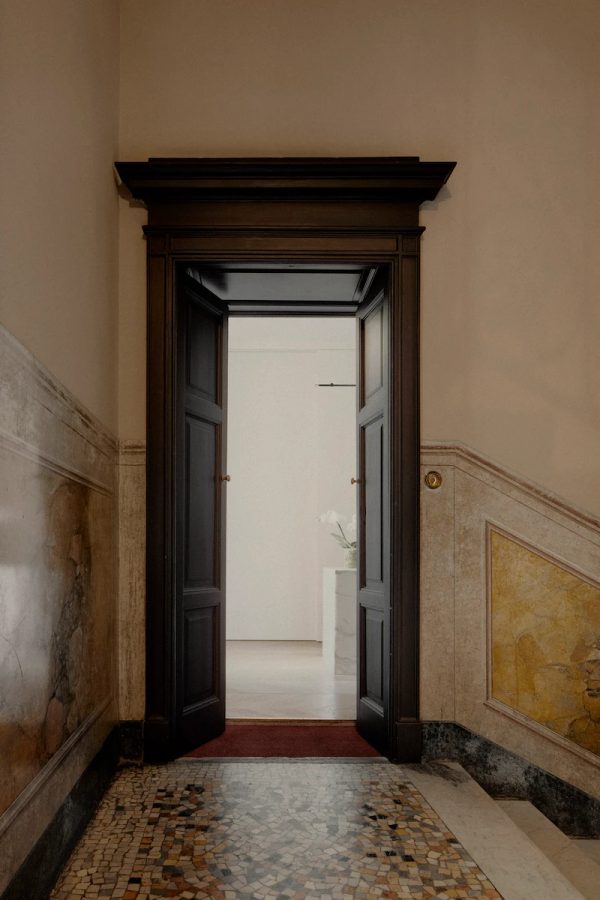 porta d’ingresso in legno scuro con dettagli architettonici classici e pavimento a mosaico, che apre su un interno moderno