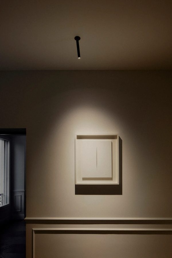 opera d’arte moderna bianca su parete illuminata da una luce diretta che crea effetto drammatico