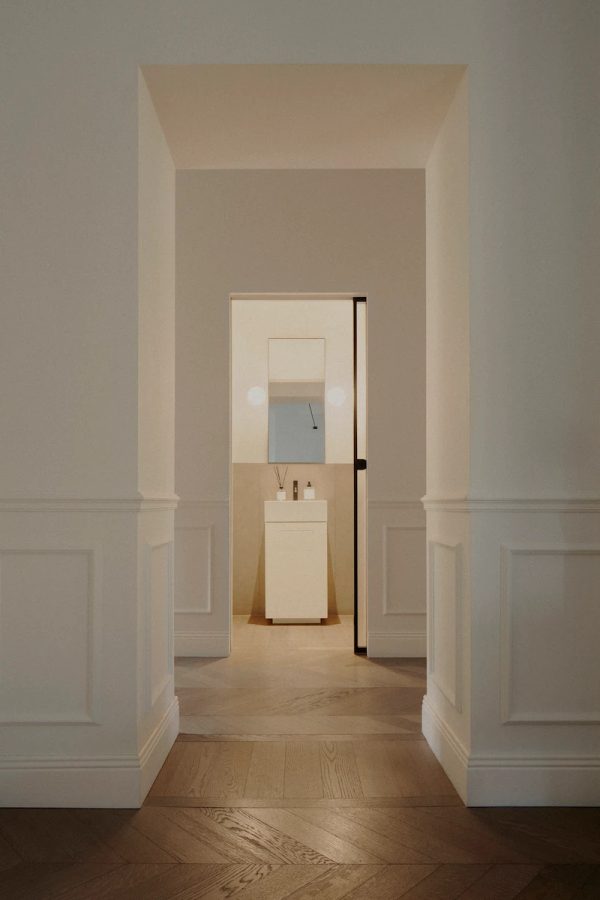 ingresso di un bagno con lavandino bianco, porta in vetro opaco, pavimento in parquet e pareti neutre