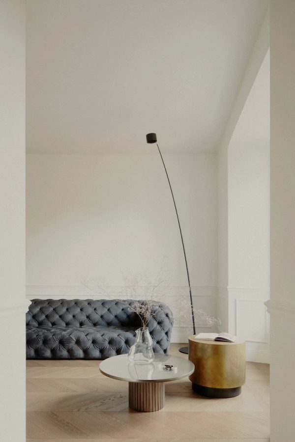 salottino accogliente con divano trapuntato in pelle nera, tavolini in ottone e marmo, lampada a stelo moderna