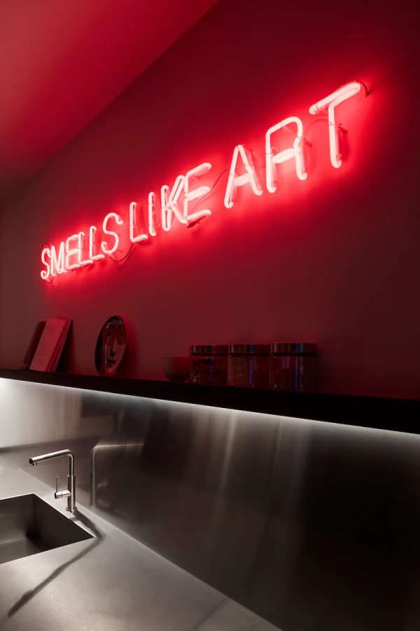 insegna al neon rossa "Smells Like Art" in una cucina moderna con piano di lavoro in acciaio e vari accessori