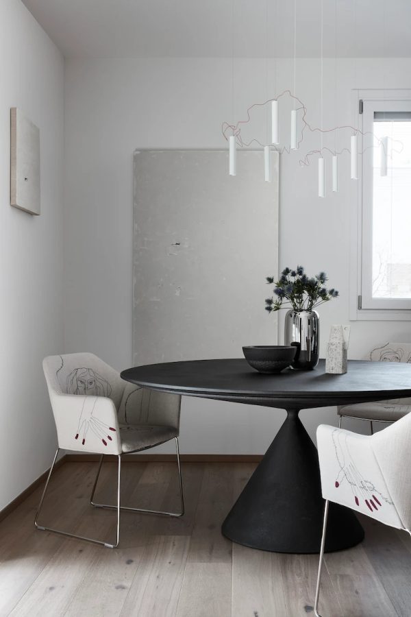 sala da pranzo moderna con tavolo rotondo nero, sedie ricamate con disegni artistici e lampadario sospeso a forma astratta