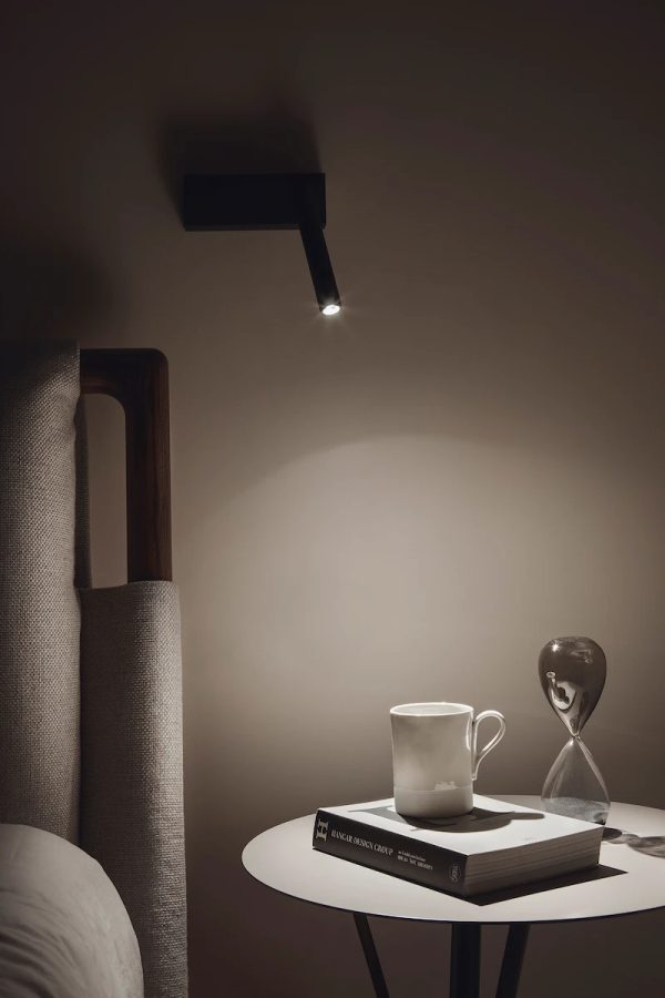 atmosfera intima in camera da letto, con una lampada orientabile e un piccolo tavolo decorato con una tazza e un libro