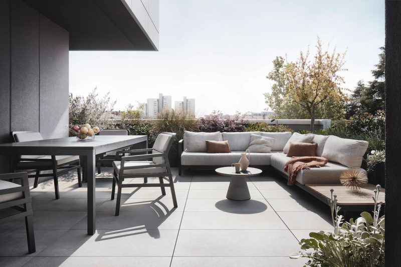 modern terrace with a corner sofa, round coffee table, dining table with chairs, ornamental plants, and panoramic city view