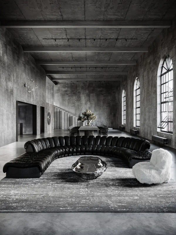 ampio loft industriale in cemento con divano in pelle a semicerchio, tavolo scultoreo in metallo e poltrona in pelo bianco