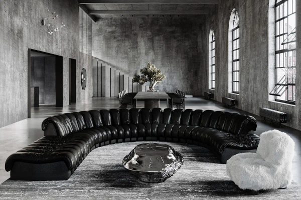 ampio loft industriale in cemento con divano in pelle a semicerchio, tavolo scultoreo in metallo e poltrona in pelo bianco
