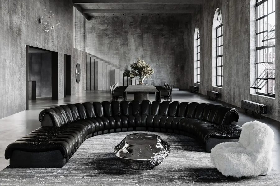 ampio loft industriale in cemento con divano in pelle a semicerchio, tavolo scultoreo in metallo e poltrona in pelo bianco