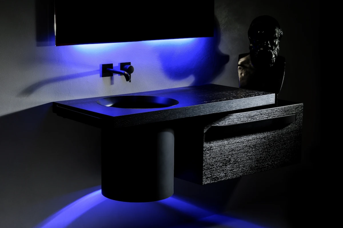 mobile da bagno moderno in legno nero con lavabo integrato e illuminazione LED blu, accompagnato da un busto classico e rubinetteria di design
