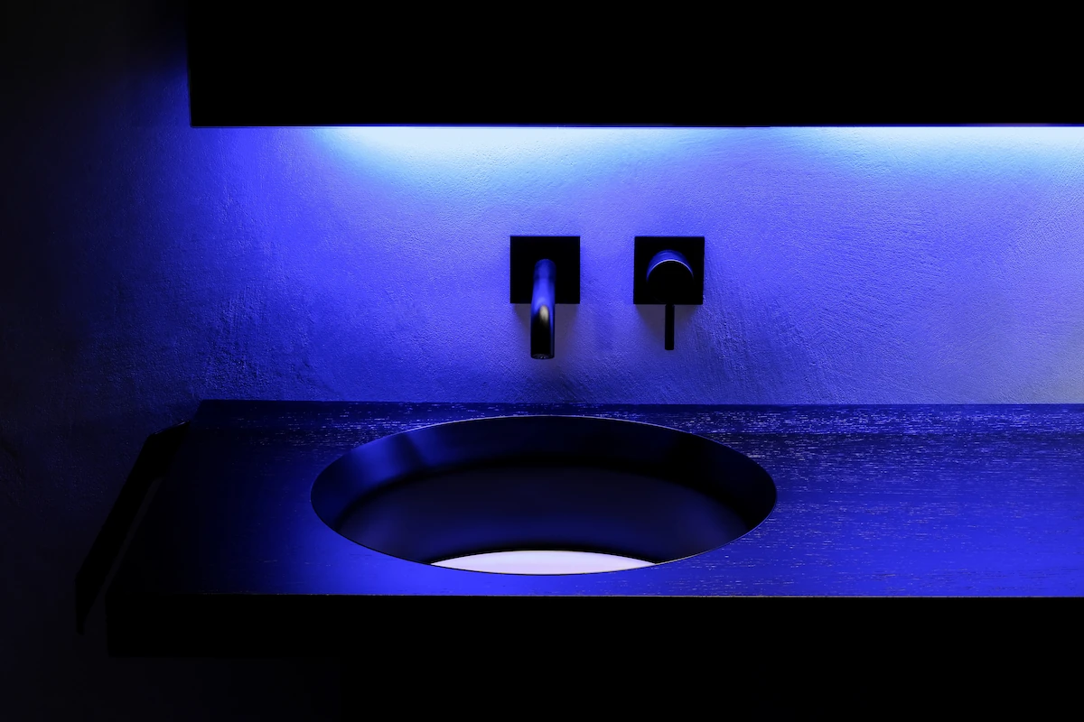primo piano di lavabo rotondo in acciaio nero, rubinetteria a parete e LED blu d’accento