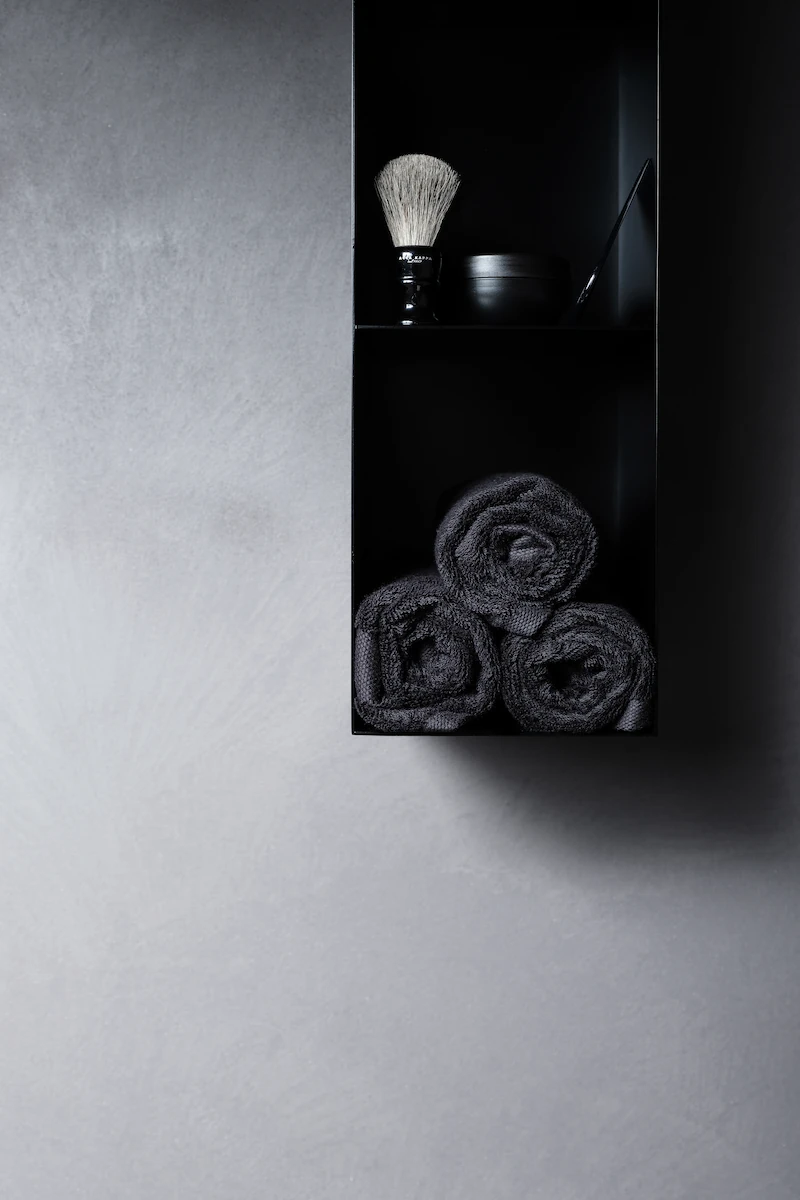 dettaglio di mensola con accessori bagno di lusso e asciugamani neri su parete grigia