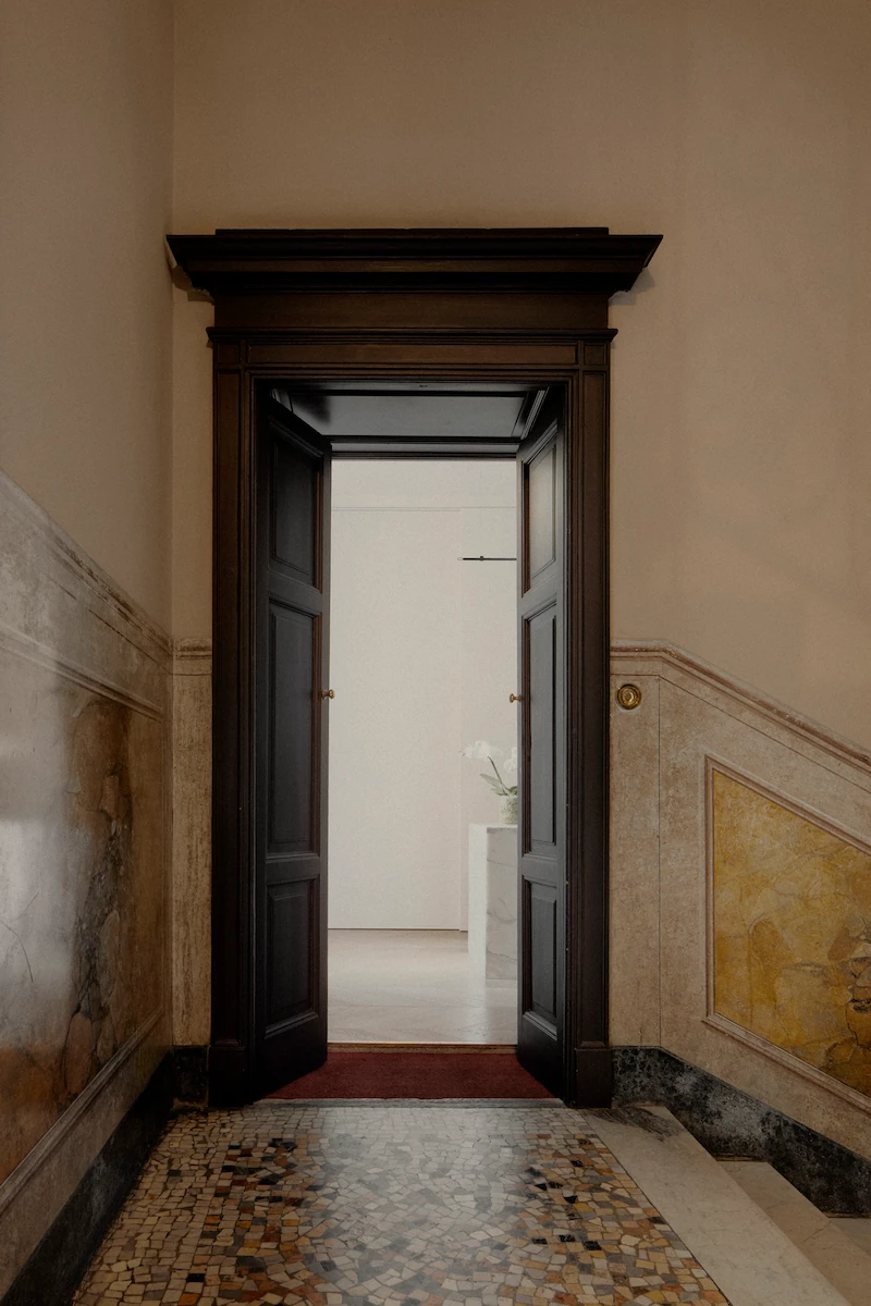 porta d’ingresso in legno scuro con dettagli architettonici classici e pavimento a mosaico, che apre su un interno moderno