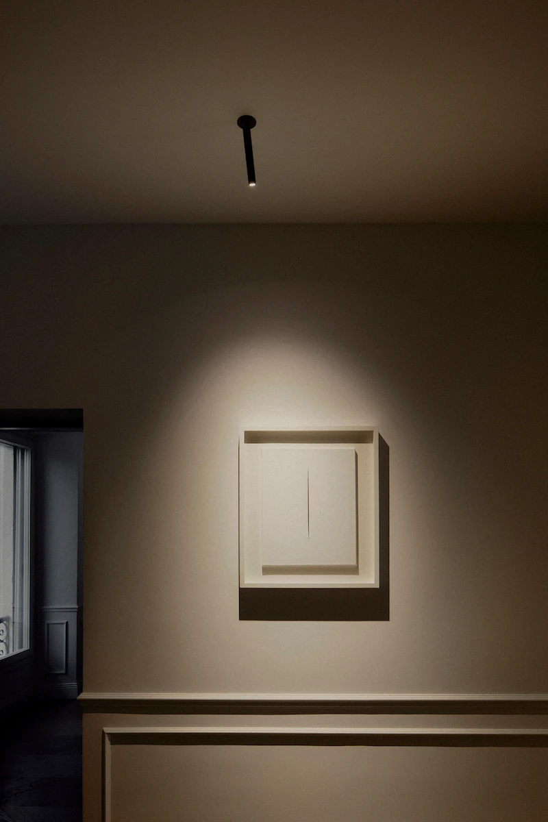 opera d’arte moderna bianca su parete illuminata da una luce diretta che crea effetto drammatico