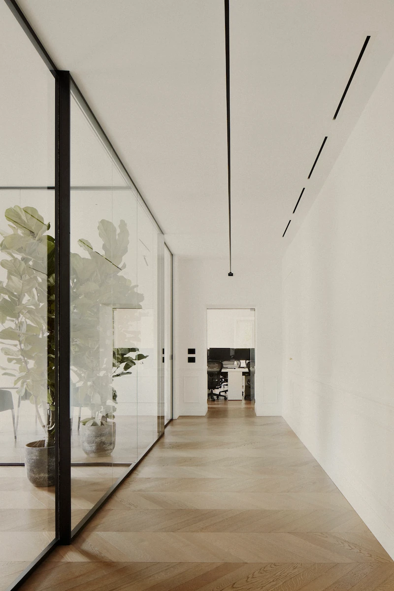 corridoio moderno con pareti vetrate a tutta altezza, parquet a spina di pesce, piante decorativa e illuminazione lineare