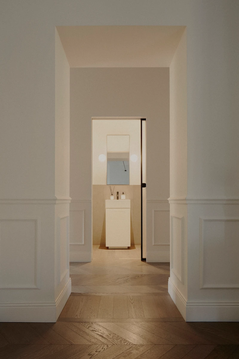 ingresso di un bagno con lavandino bianco,porta in vetro opaco, pavimento in parquet e pareti neutre