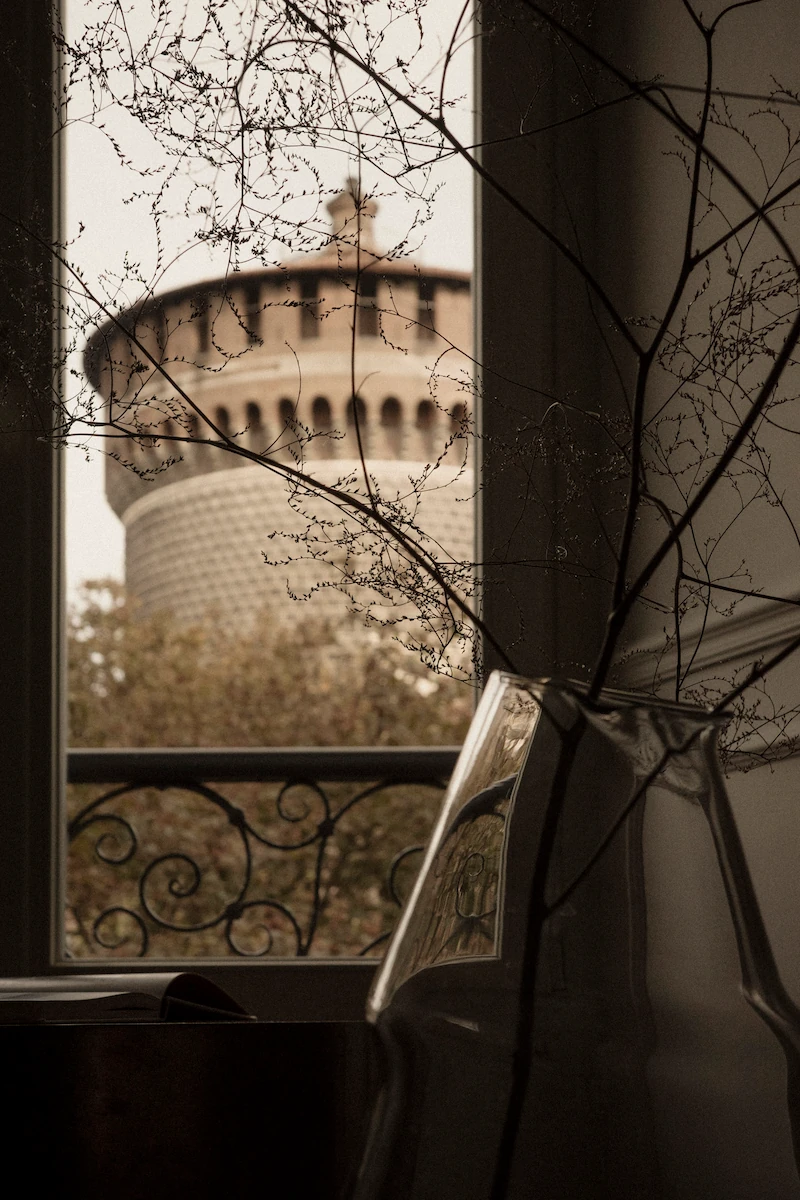 finestra con ringhiera in ferro battuto e vista su una torre del Castello Sforzesco, con pianta decorativa