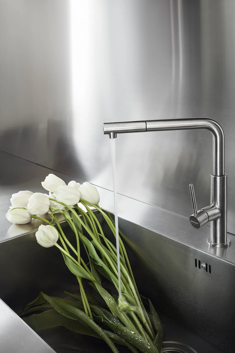 lavello cucina moderno in acciaio inox con tulipani bianchi freschi e acqua che scorre da un rubinetto di design in acciaio