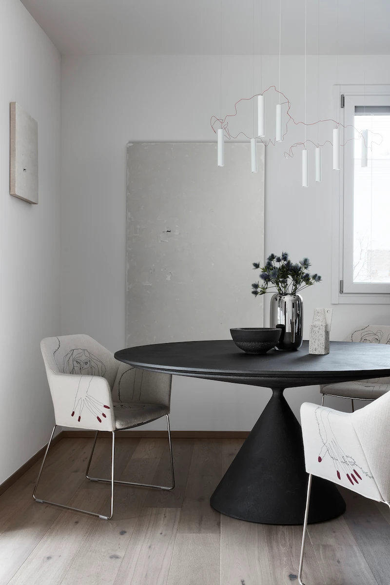 sala da pranzo moderna con tavolo rotondo nero, sedie ricamate con disegni artistici e lampadario sospeso a forma astratta