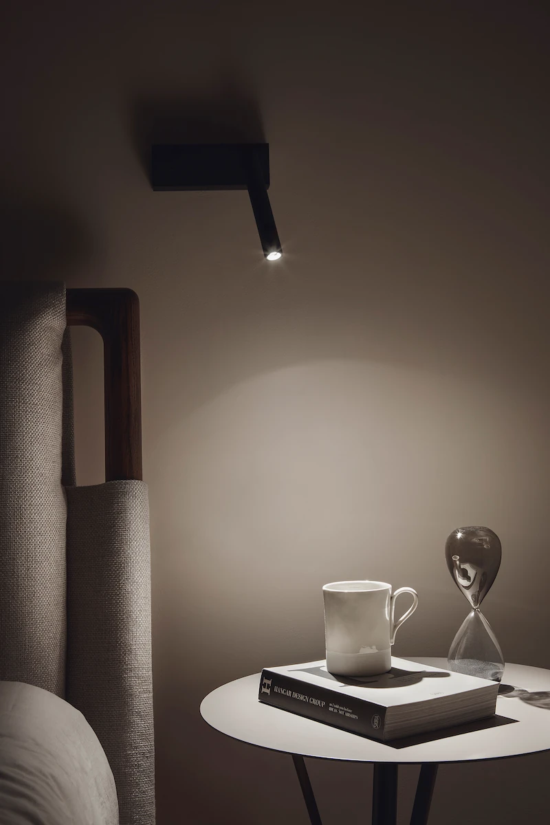 atmosfera intima in camera da letto, con una lampada orientabile e un piccolo tavolo decorato con una tazza e un libro