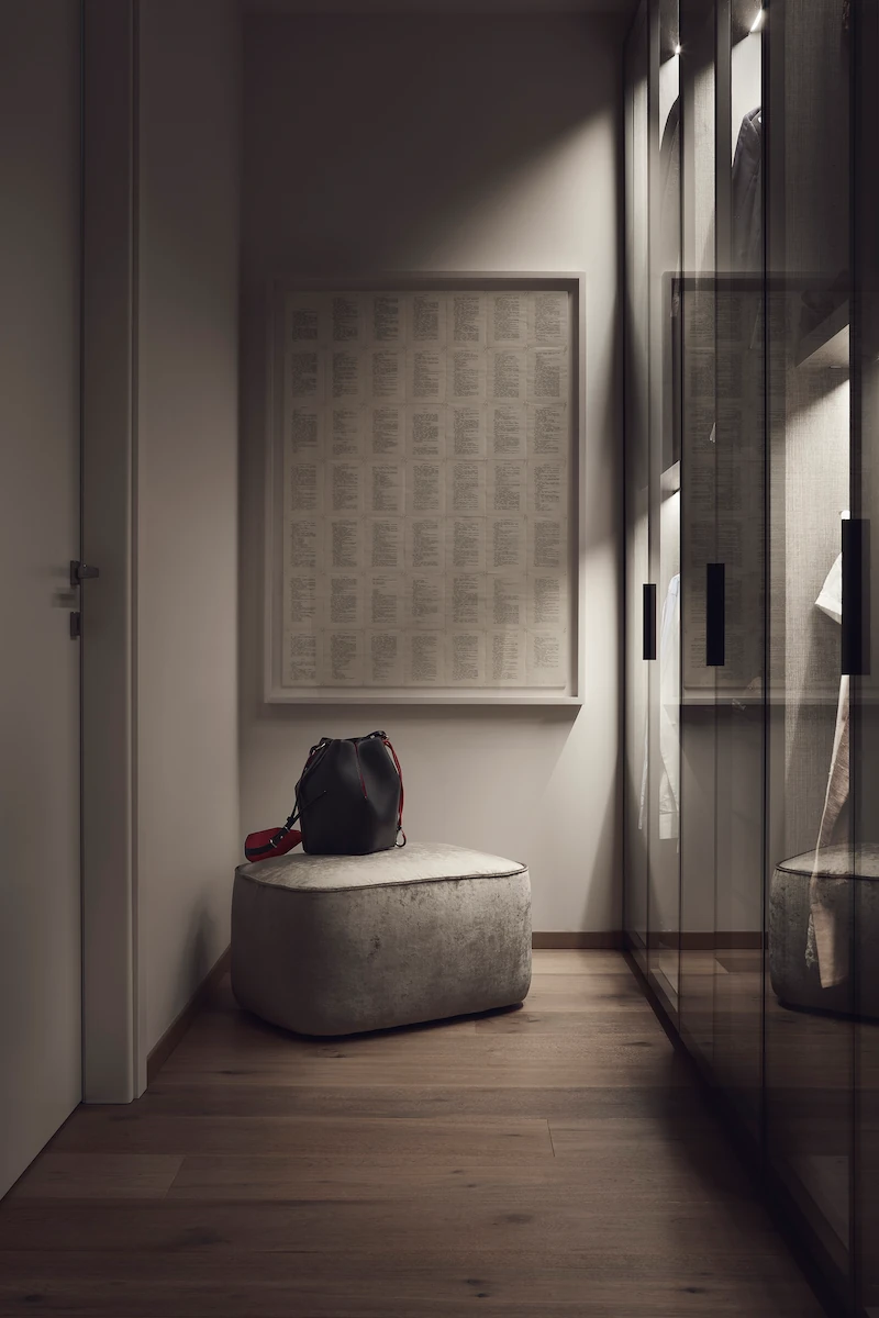 angolo guardaroba con armadi a vetri, un pouf imbottito e una borsa nera, illuminato da luce soffusa