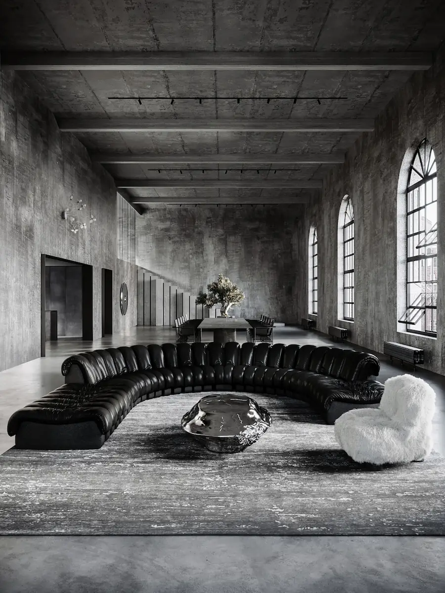 ampio loft industriale in cemento con divano in pelle a semicerchio, tavolo scultoreo in metallo e poltrona in pelo bianco