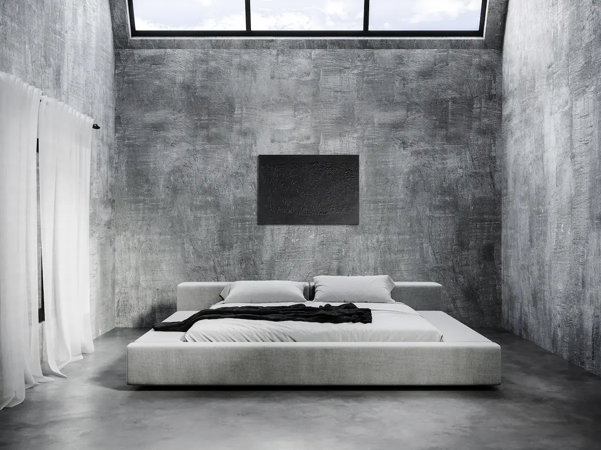 camera da letto con pareti in cemento, letto a piattaforma in stile giapponese in tessuto chiaro e opera d’arte astratta nera