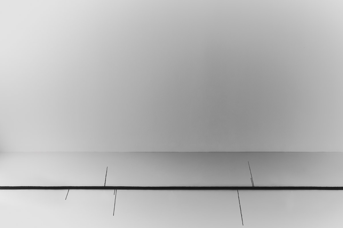 tappeto in seta lineare con sottili frange artistiche, affiancato a un busto classico bianco su uno sfondo grigio